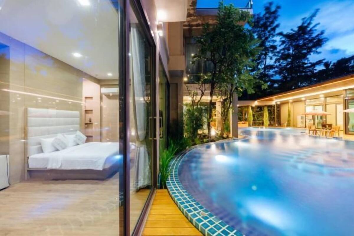 A modern hotel room with a glass wall, a bed, and a view of an infinity pool.