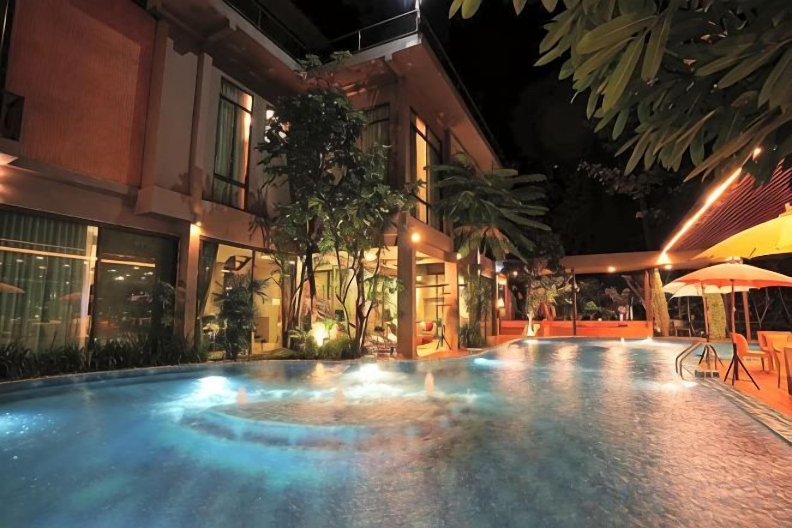 Una piscina interior con zonas de descanso alrededor, un área de estar techada y un edificio con grandes ventanales.