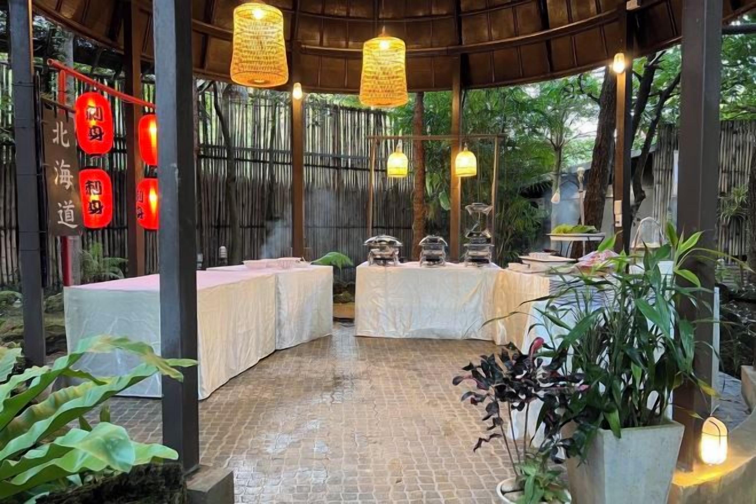 Un espacio de comedor al aire libre techado con mesas, luces colgantes y faroles rojos.
