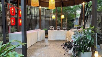 Un espacio de comedor al aire libre techado con mesas, luces colgantes y faroles rojos.