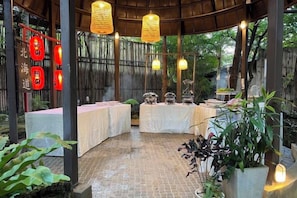 Un espace extérieur abrité, aménagé pour les repas, avec des tables, des guirlandes lumineuses et des lanternes rouges.