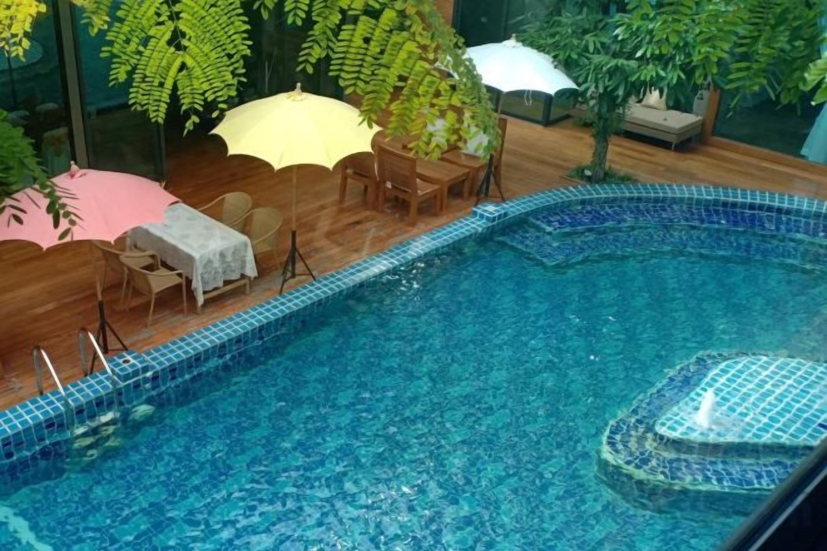 Una piscina interior con bordes de azulejos, rodeada de mobiliario de madera y sombrillas.
