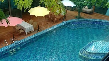 Una piscina interior con bordes de azulejos, rodeada de mobiliario de madera y sombrillas.