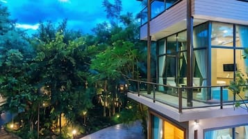 A modern multi-story building with glass balconies, surrounded by lush greenery.