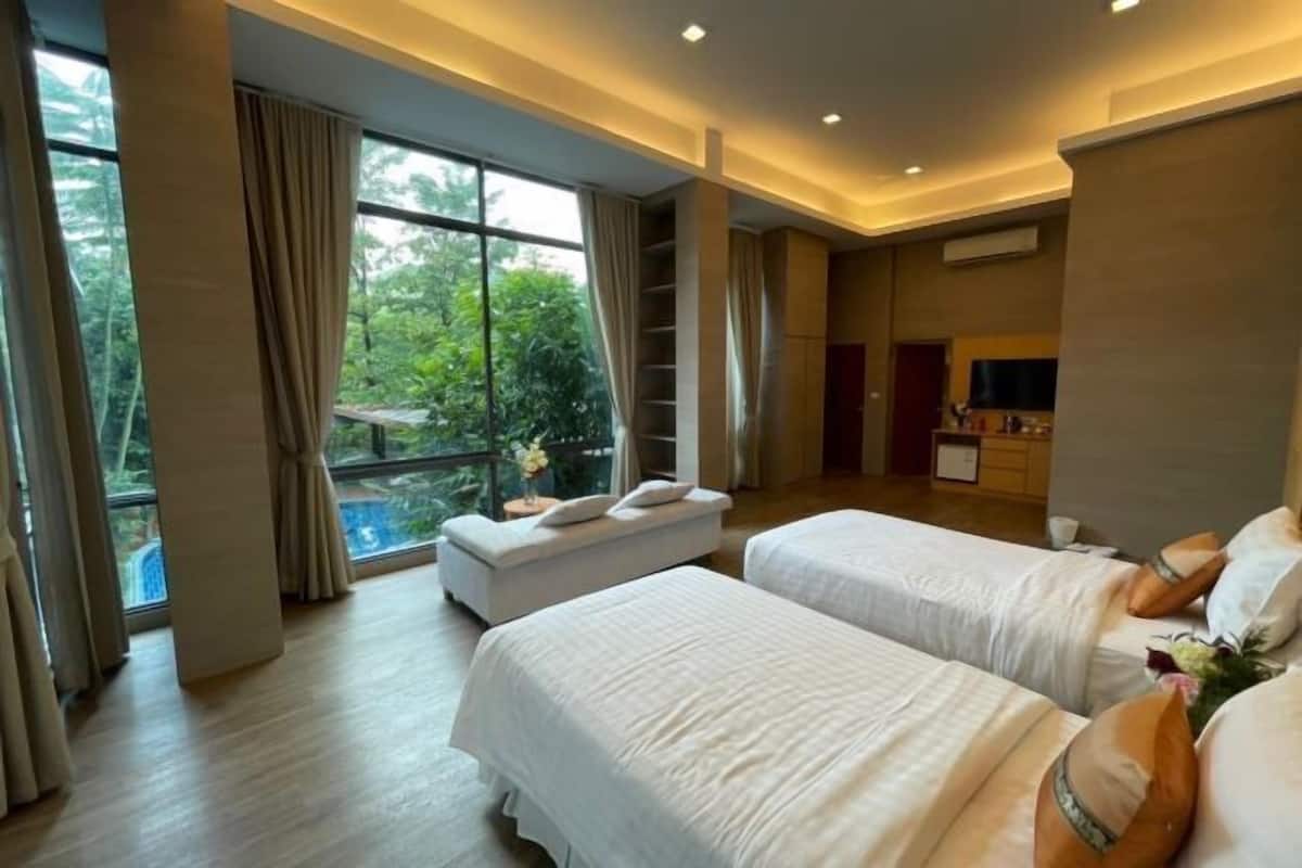 A hotel room with two beds, a sofa, a TV, and a balcony with a view of greenery.