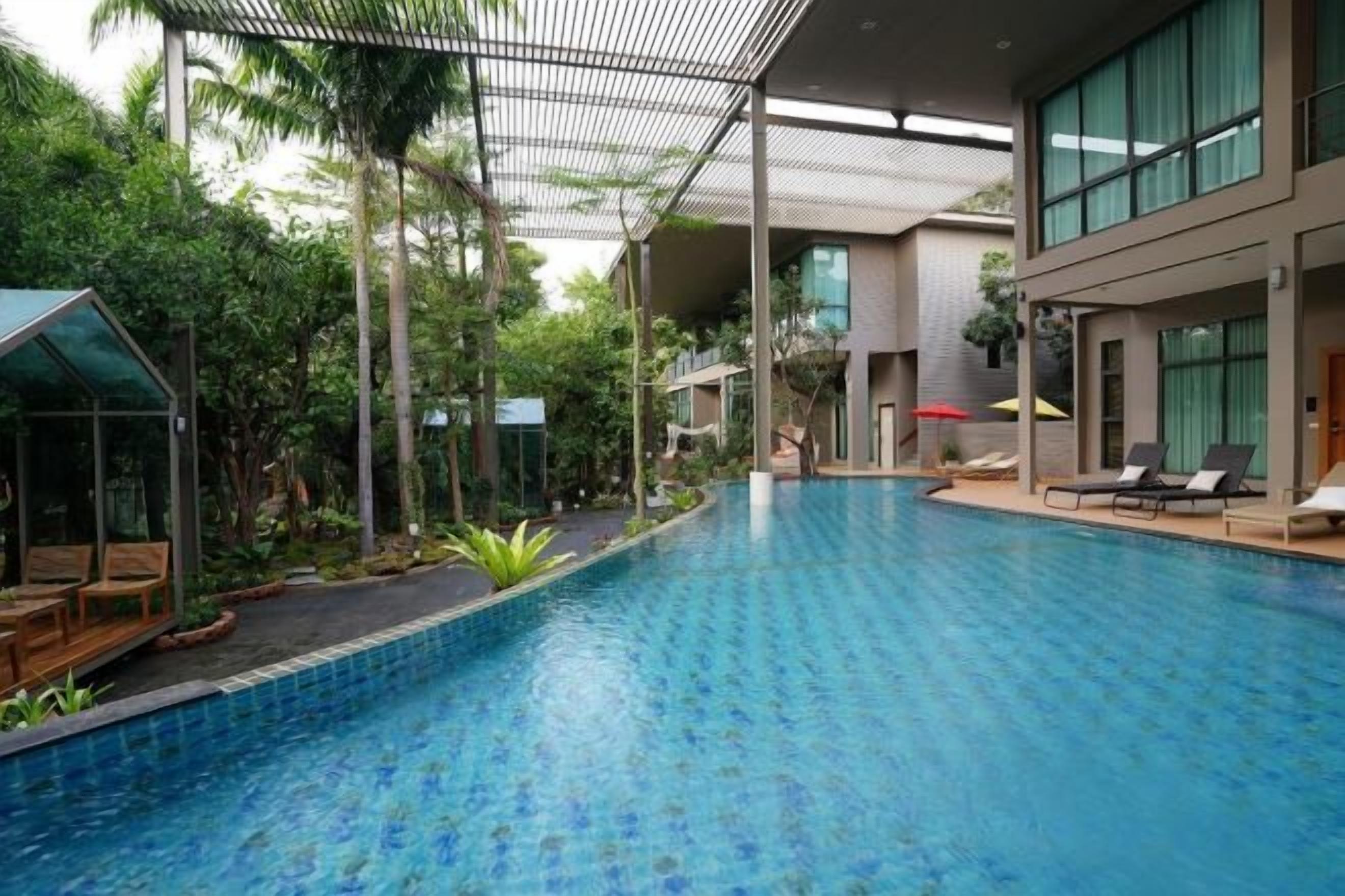 An indoor swimming pool with a modern design, surrounded by greenery and a covered area with seating.