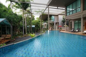 Una piscina interior con diseño moderno, rodeada de vegetación y una zona cubierta con asientos.