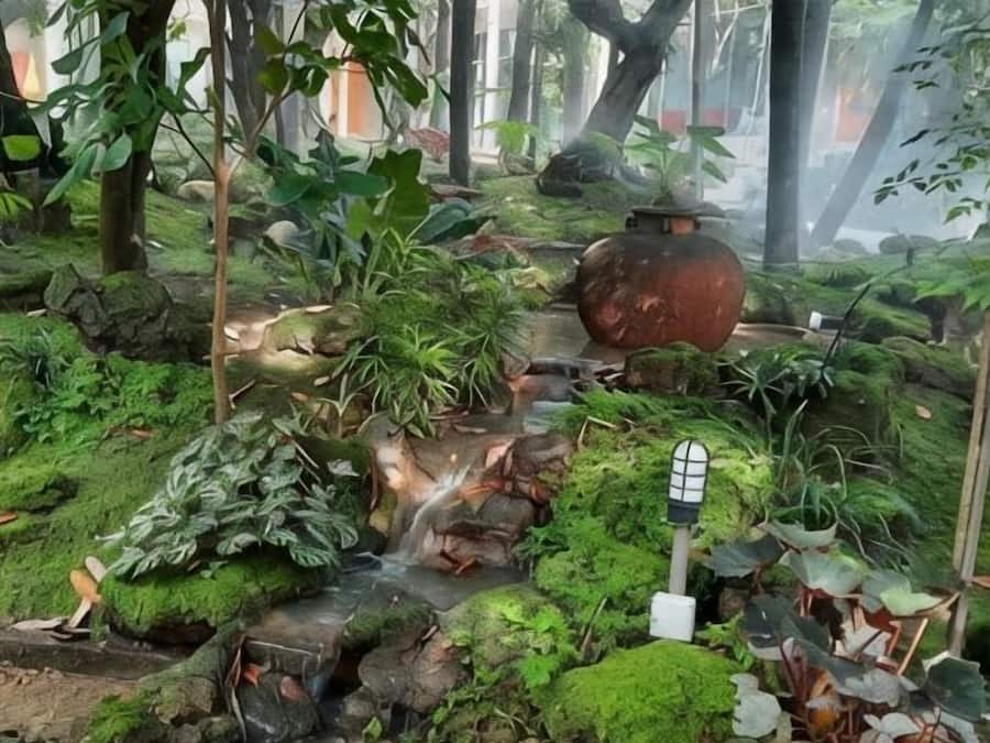 A lush garden with a small waterfall, a large pot, and a signpost.