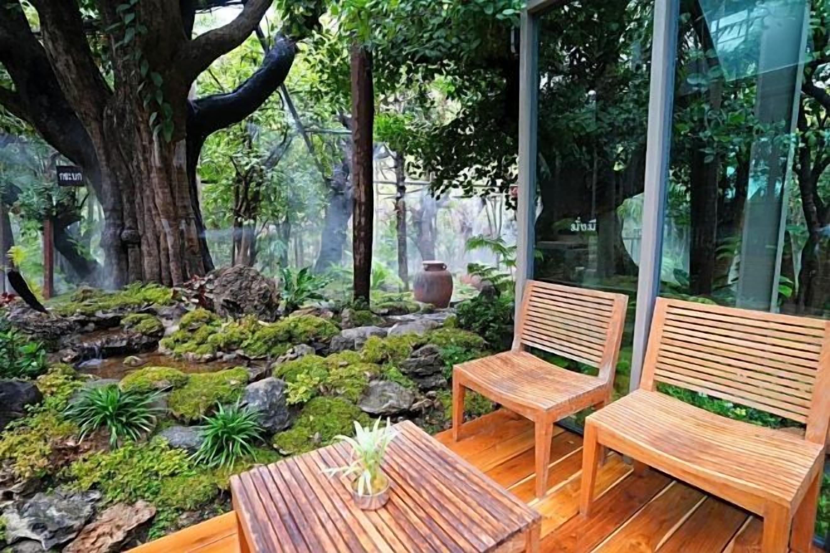 Un conjunto de banco y mesa de madera en un jardín con un árbol grande y una cascada pequeña.