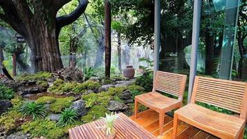 Un conjunto de banco y mesa de madera en un jardín con un árbol grande y una cascada pequeña.