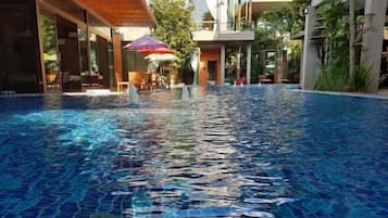 Una piscina con agua cristalina, rodeada de asientos exteriores y sombrillas, lo que sugiere un entorno de resort.