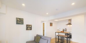 A modern living room with a grey sofa, a small table with stools, and artwork on the walls.
