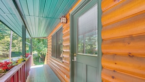 Une cabane en bois avec un porche, une porte verte et une fenêtre avec des stores.