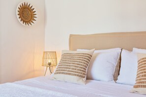 Een net opgemaakt bed met witte beddengoed en gestreepte kussens, een ronde wanddecoratie en een kleine lamp op een nachtkastje.