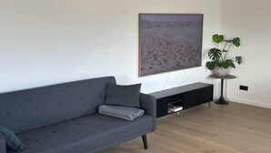 A modern living room with a grey sofa, a black entertainment unit, a large framed picture on the wall, and a potted plant. - Privatunterkunft in Wendisch Rietz, Deutschland (Wendisch Rietz)