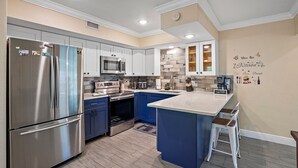 A modern kitchen with stainless steel appliances, blue cabinets, and a central island with bar stools.