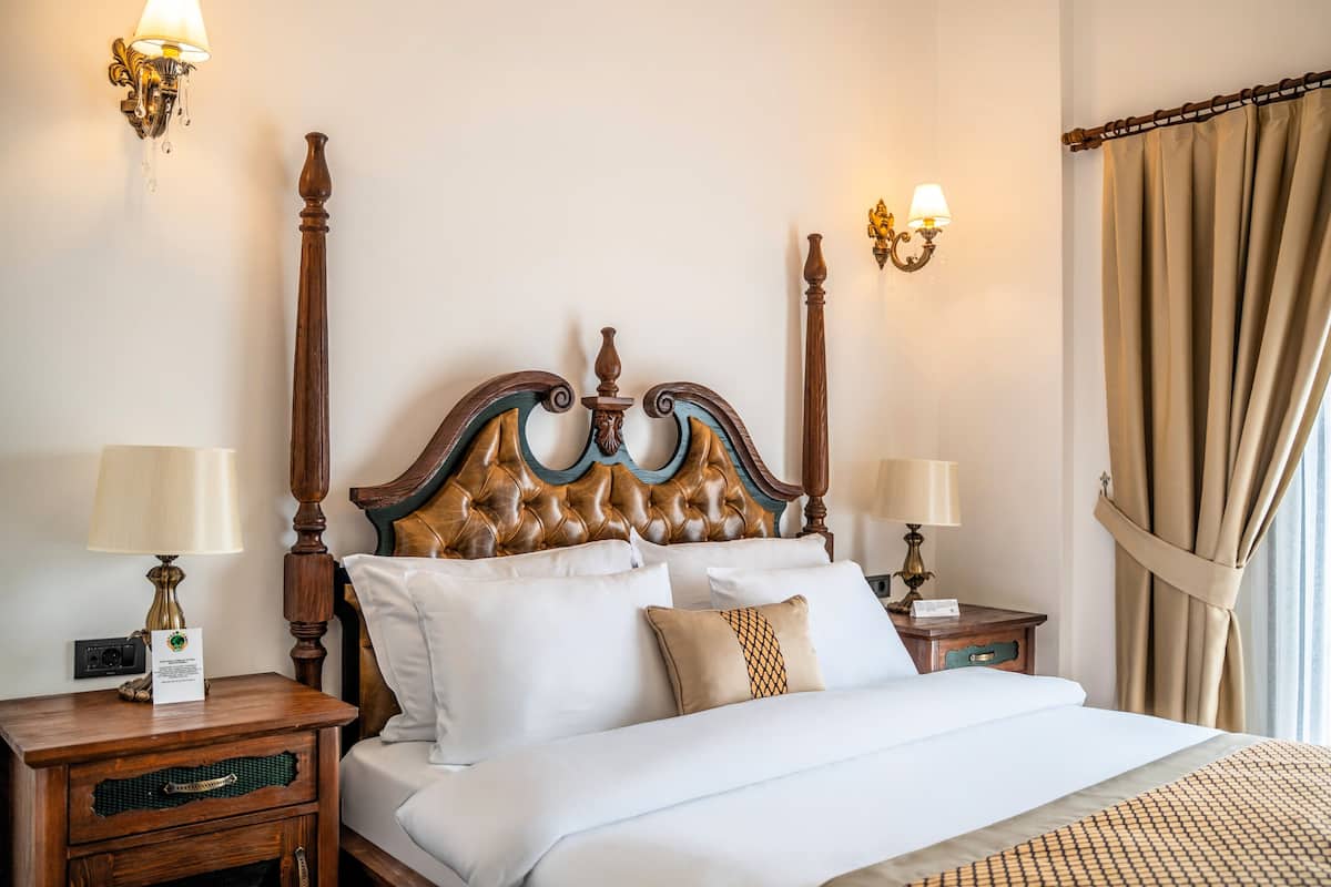 A neatly made bed with a wooden headboard, two bedside tables with lamps, and a curtain on the window.