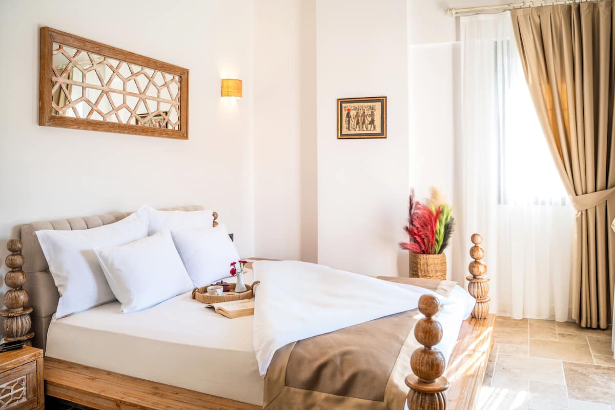 A neatly made bed with white linens, a wooden headboard, and a bedside table with a tray.