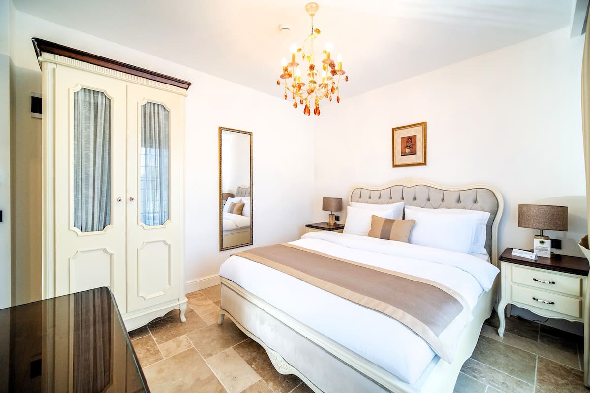 A neatly arranged bedroom with a large bed, bedside tables, a wardrobe, and a chandelier.