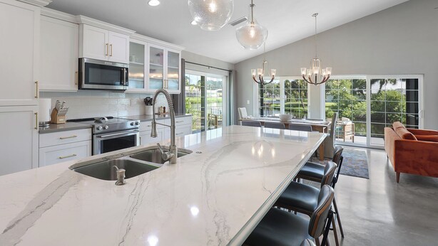 Una cocina moderna con armarios blancos, electrodomésticos de acero inoxidable y una isla grande con un lavamanos.
