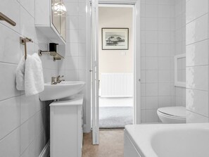 A modern bathroom with a white sink, toilet, and bathtub. A towel hangs on a rack, and a framed picture is visible on the wall.
