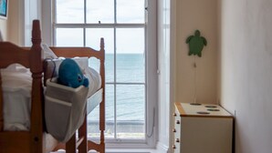 Ein Zimmer mit Blick auf das Meer durch ein großes Fenster, einem hölzernen Bett, einer kleinen Kommode und einer Wanddekoration mit einer grünen Schildkröte.