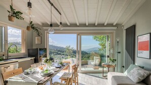 Un coin repas avec une table dressée pour quatre personnes, un canapé et une vue sur un paysage montagneux, visible à travers de grandes portes vitrées.