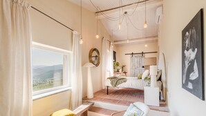 Une pièce avec une grande fenêtre, un lit, un banc et une chaise. La fenêtre offre une vue sur l’extérieur.