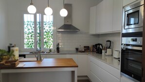 A modern kitchen with white cabinets, a wooden countertop, a stainless steel range hood, and a built-in oven.