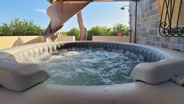 An outdoor hot tub with a canopy, surrounded by stone walls and greenery.