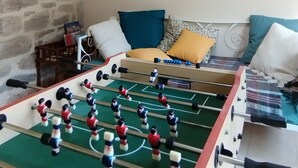 A room with a foosball table, stone wall, wooden beams, a mirror, a clock, and a sofa with cushions. - La Cireygeade (St Martial de Gimel)
