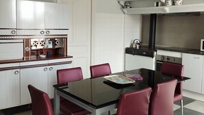 A modern kitchen with white cabinetry, a black countertop, and a dining area with a glass table and red chairs. - La Cireygeade (St Martial de Gimel)