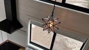 A modern kitchen with a built-in window, a star-shaped hanging light, and a black range hood. - Unit #5 - Modern Tiny Home in the heart of TX Wineries (Johnson City)