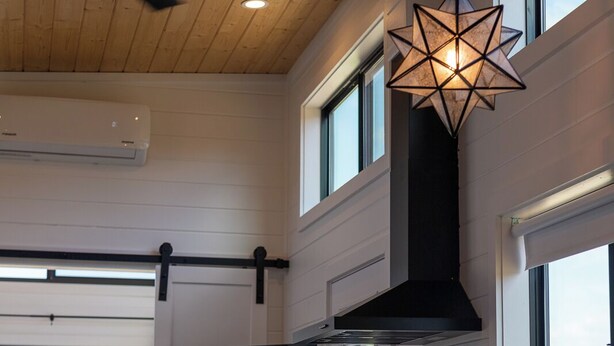 A modern kitchen with a high ceiling, a ceiling fan, a black range hood, a large window, and a TV mounted on the wall. - Unit #5 - Modern Tiny Home in the heart of TX Wineries (Johnson City)
