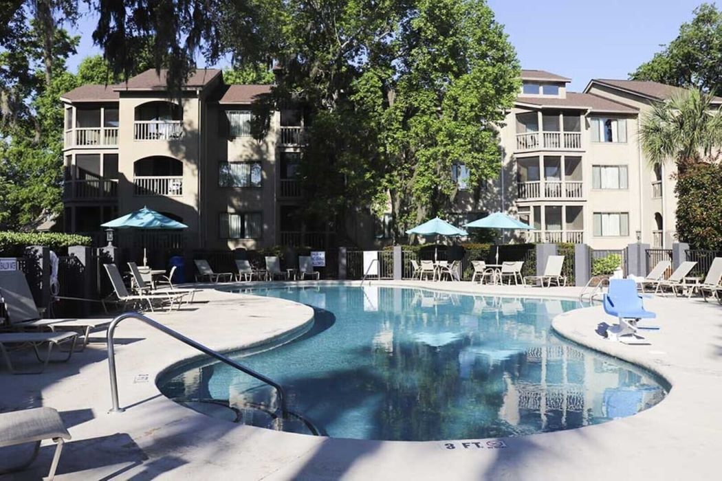 Une piscine entourée de bâtiments à plusieurs étages dotés de balcons, avec des chaises longues et des parasols à proximité.