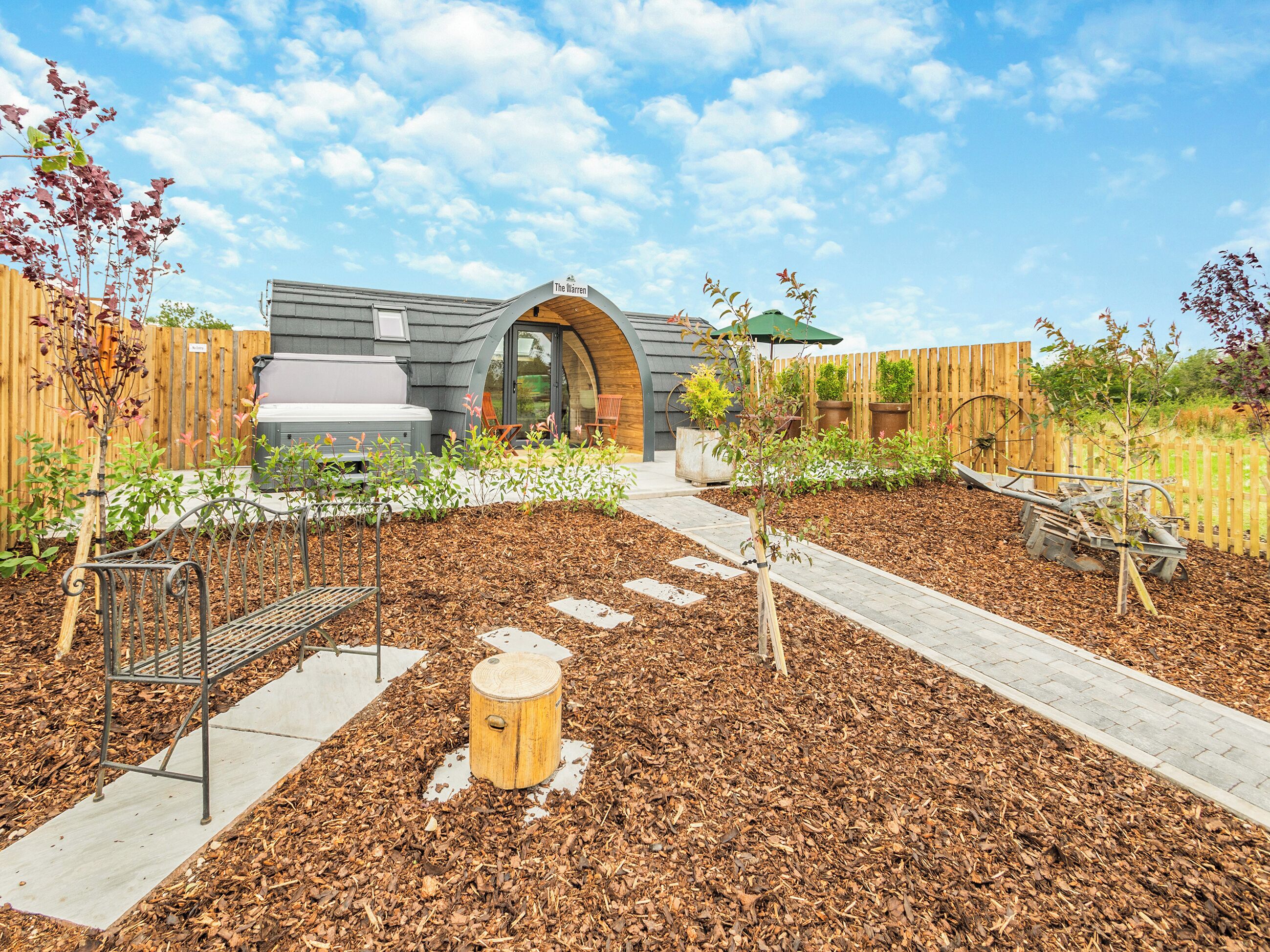 Un jardín con un banco de madera, piedras para caminar y un poste de madera.