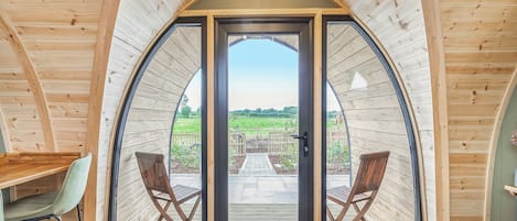 Une pièce accueillante, partiellement ouverte, avec des murs en bois et une grande porte vitrée donnant sur un espace extérieur. À l’intérieur, on trouve une table en bois et deux chaises.