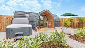 A modern, curved building with a sign reading "The Warren." It features a hot tub, wooden deck, and potted plants.