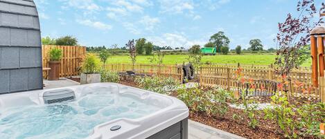 Un jacuzzi en un patio trasero con una valla de madera, una terraza de madera y un campo de césped al fondo.