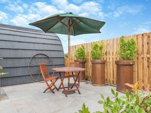 A patio with a table and chairs, a large umbrella, and potted plants against a wooden fence. - The Warren - UK47582 (Church Broughton, near Derby)