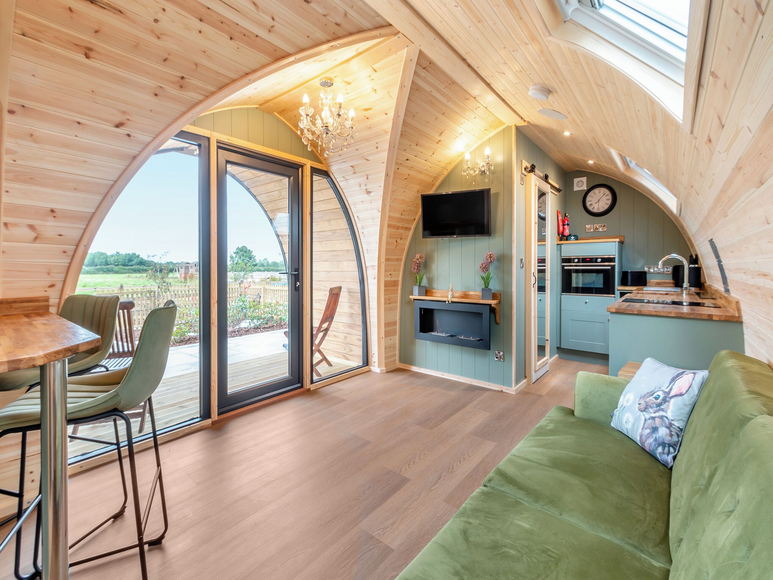 Een gezellig, gebogen houten interieur met een eethoek, een groene bank en een keuken met televisie en klok.