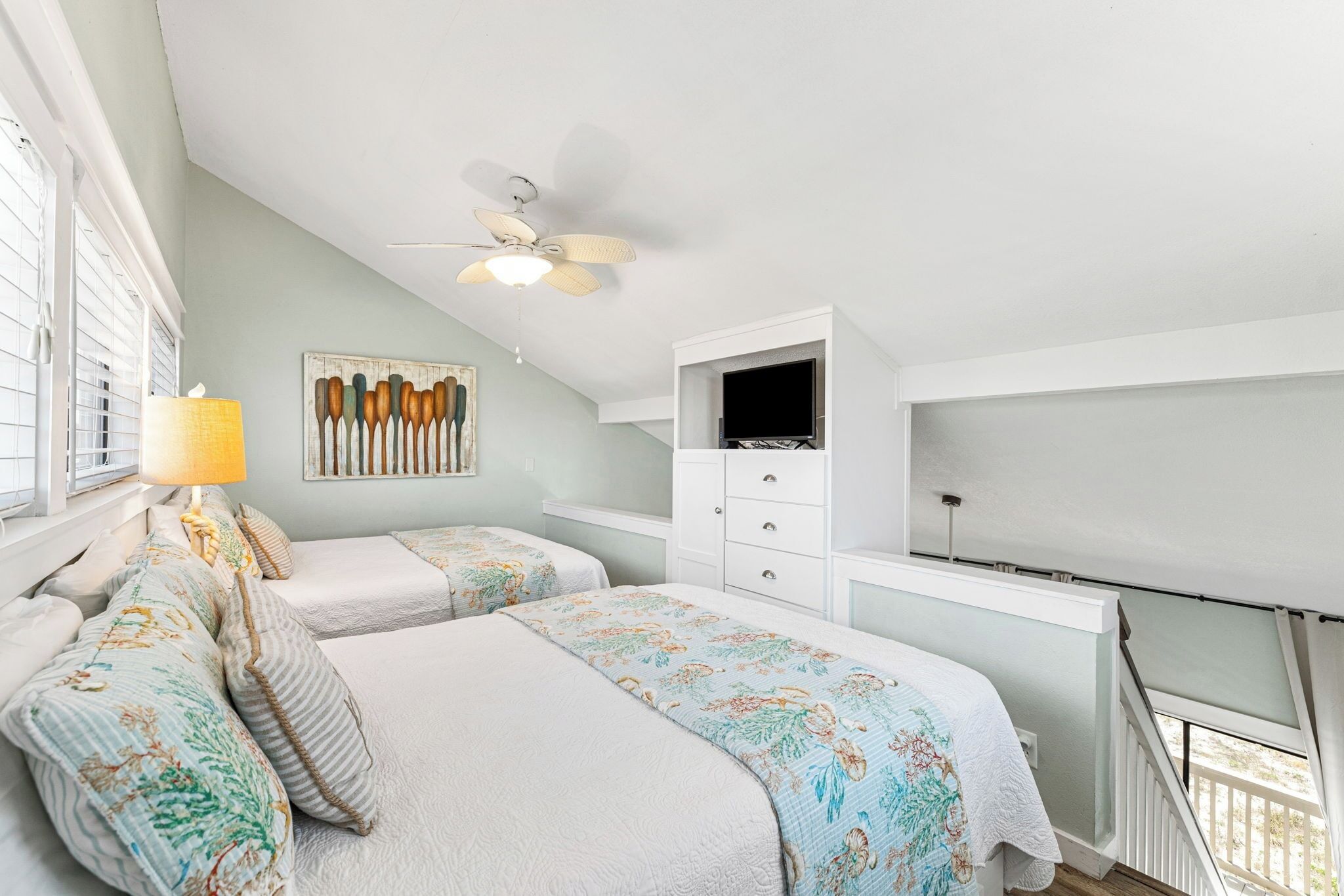 A bedroom with two beds, a ceiling fan, a TV, and a window with blinds.