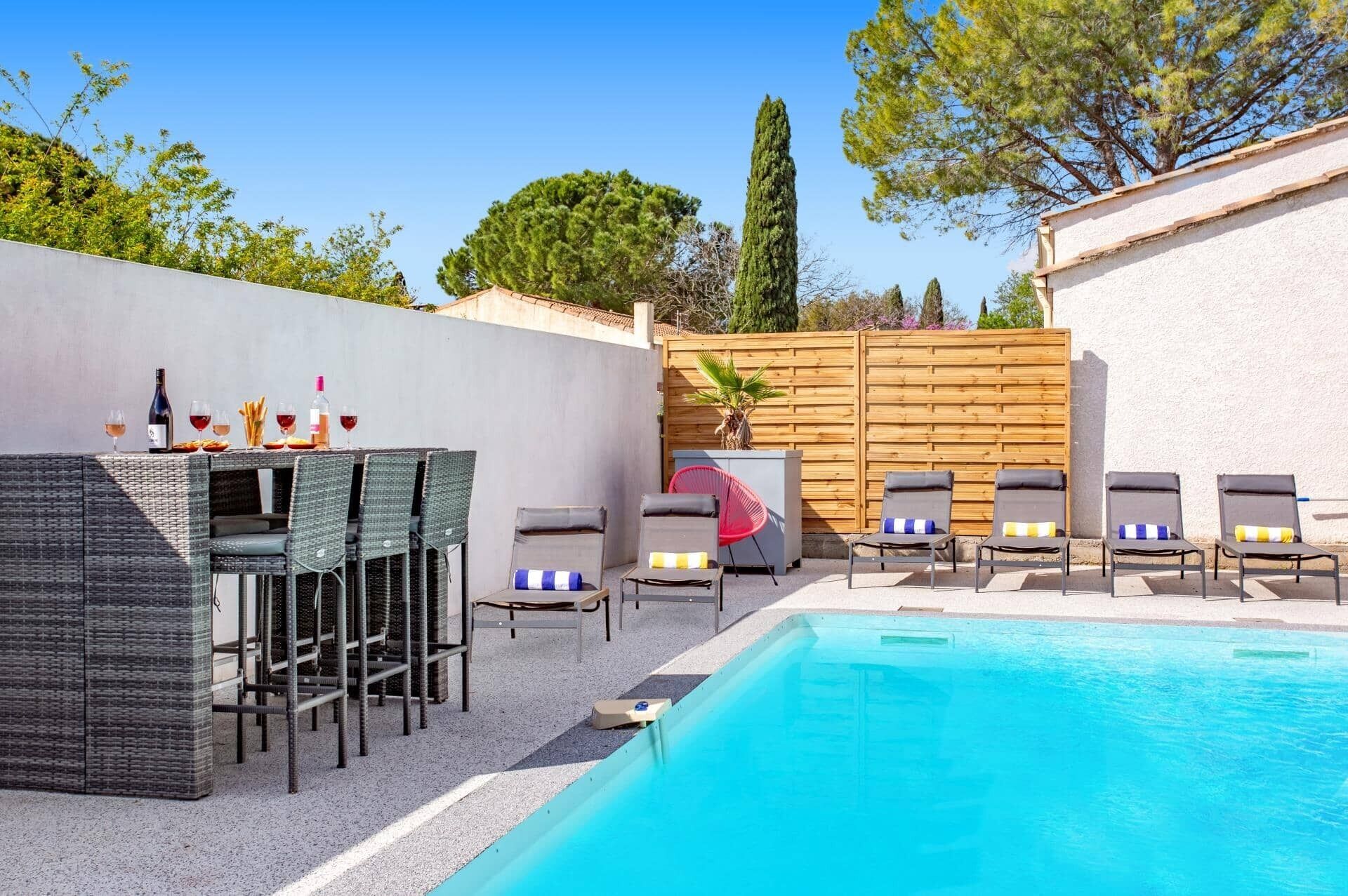 A poolside area with a table set for dining, lounge chairs, and a wooden fence.