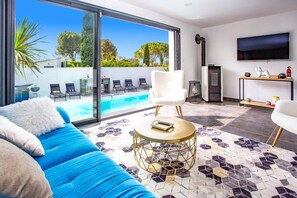 A modern living room with a pool, a white sofa, a round coffee table, and a TV on the wall.