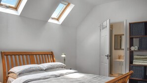 A bedroom with a sloped ceiling, skylights, a wooden bed frame, and a built-in shelving unit with folded towels. - 1 bedroom accommodation in Nether Wallop, Stockbridge (Nether Wallop, Stockbridge)