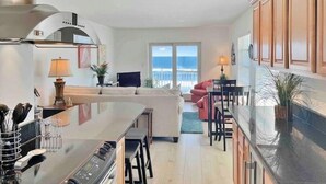 Eine moderne Küche mit Kochinsel, ein Essbereich mit Barhocker und ein Wohnzimmer mit Sofa und Meerblick.