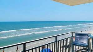 Blick auf einen Strand von einem Balkon mit Geländer, einem Stuhl und einem Tisch.