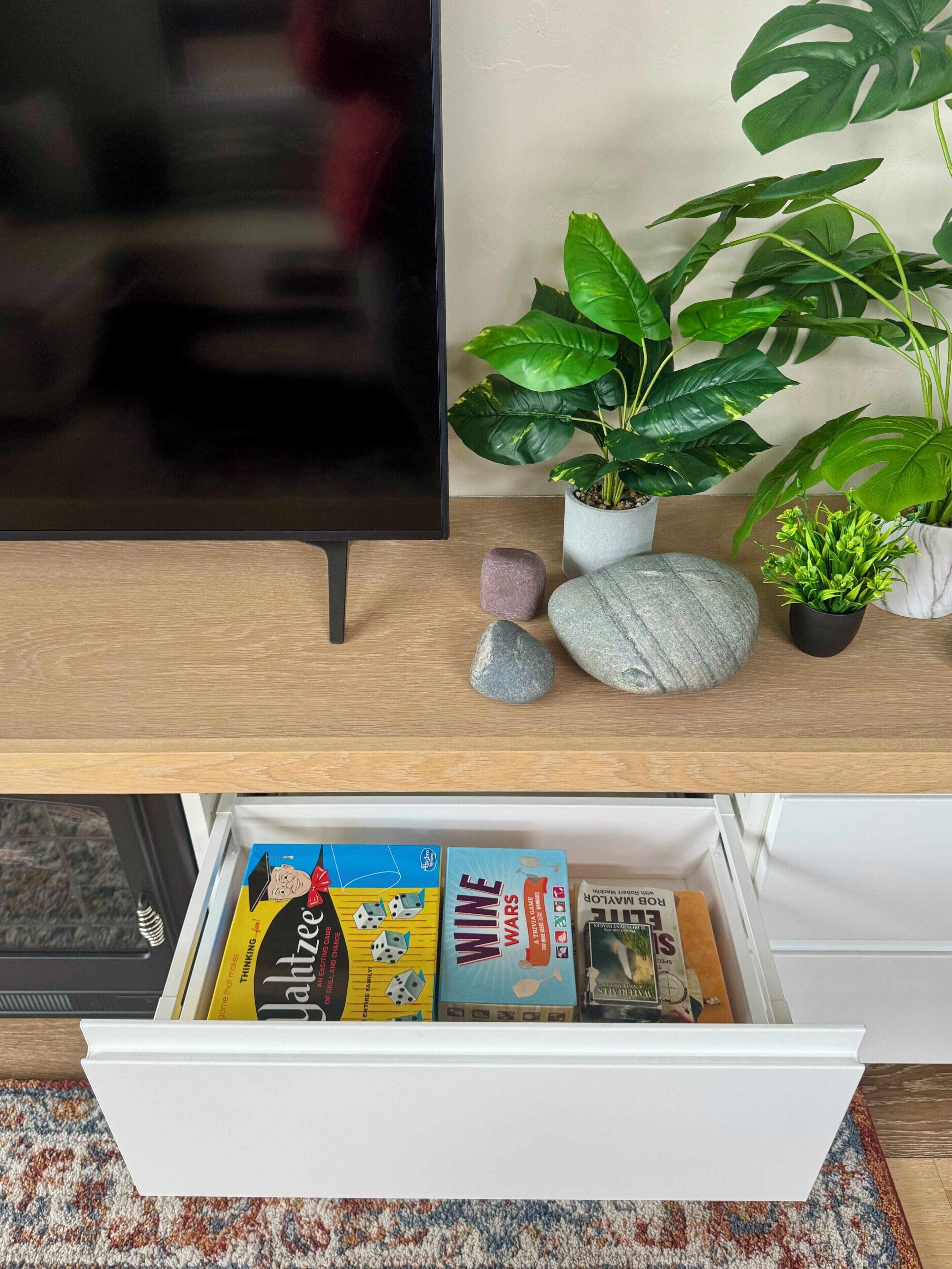 A wooden desk with a television, a potted plant, and a drawer containing books and a Rubik's Cube.