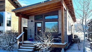 A modern wooden house with a covered porch, large windows, and a snow-covered landscape. - Cozy 2 Bedroom by Teton Pass (Victor)