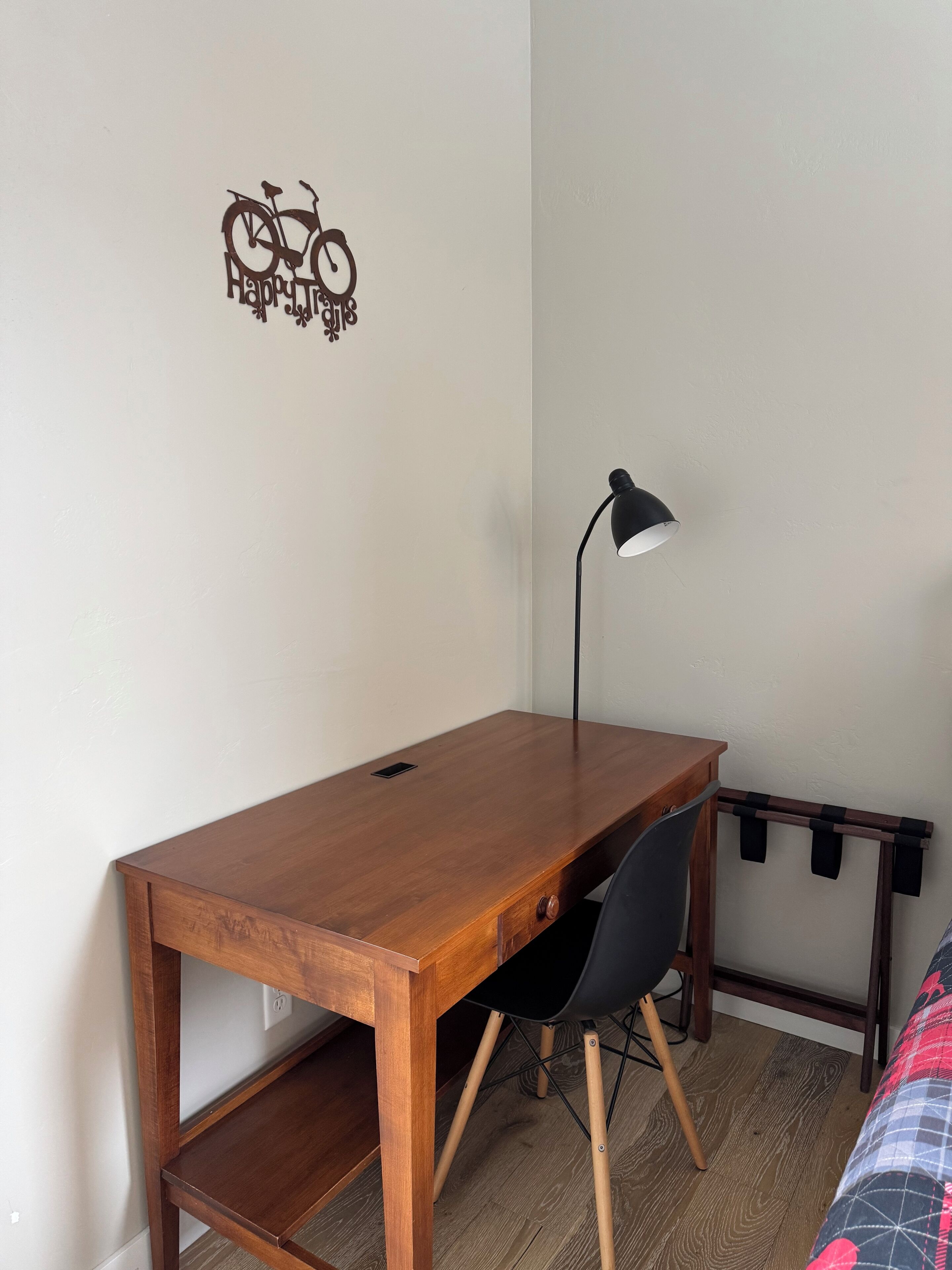 A small, neatly organized room with a wooden desk, a black chair, a desk lamp, and a wall decal of a bicycle.